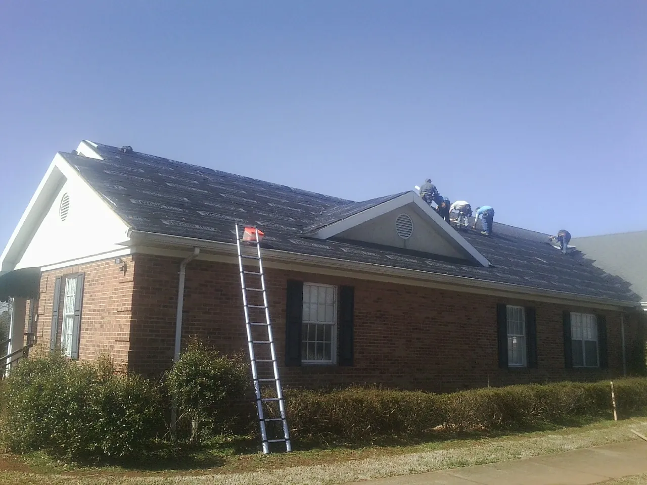Crew tearing shingles off a brick ranch roof with a ladder set — Metal Roof Repair work by our crew in Middlesex