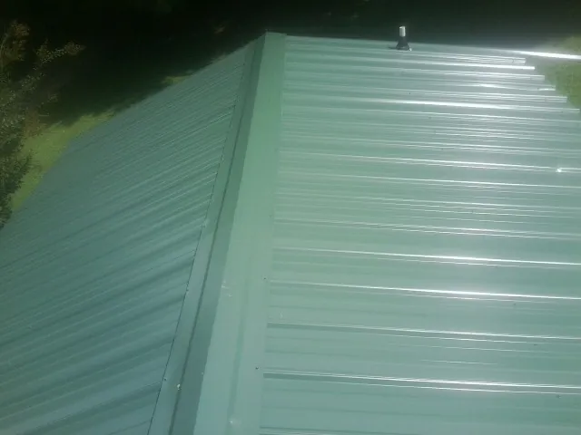 New green metal panels meeting at the ridge of a roof — Flat Roof Repair work by our crew in Middlesex