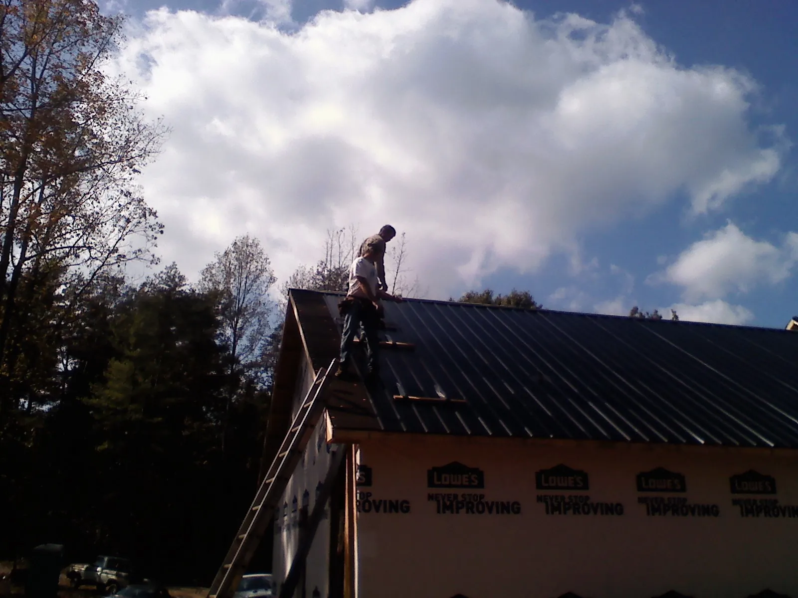 Roofer fastening dark metal panels high against a cloudy sky, from a Roof Inspection job in Middlesex