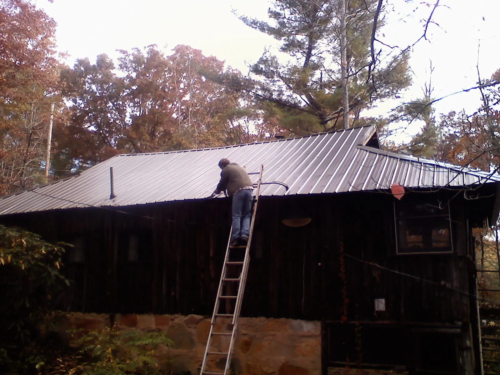 Roofer on a ladder working along the edge of a cabin metal roof in Middlesex